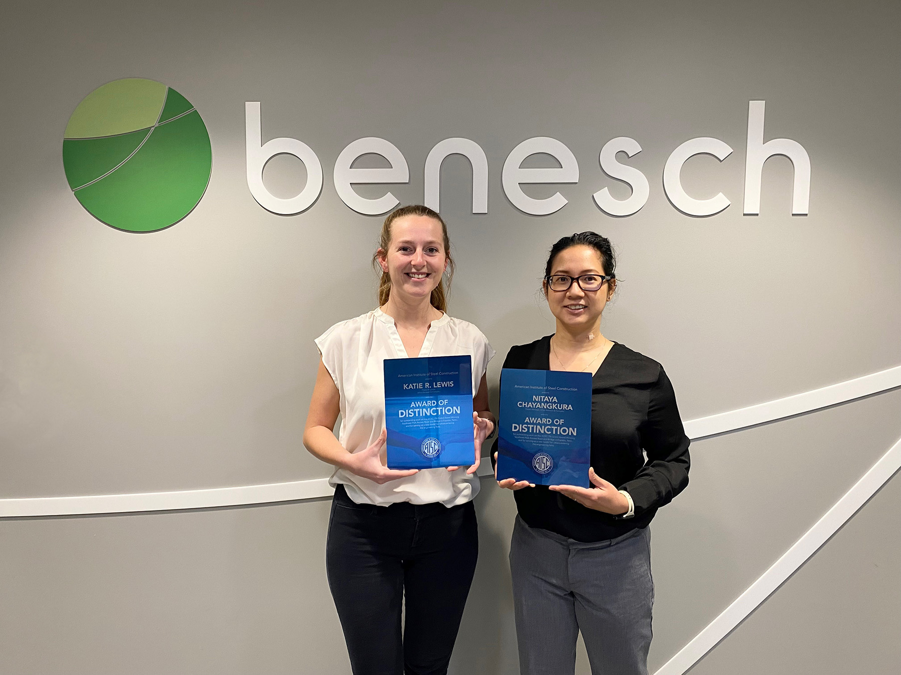 A photo of Katie and Nitaya holding awards in front of Benesch sign