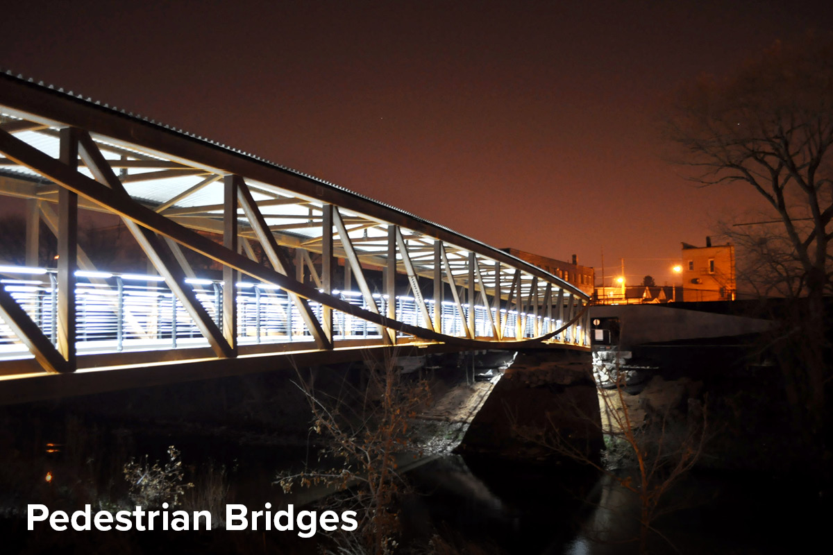 night time photo of a pedestrian bridge in Three Bridges Park in Milwaukee, with decorative lighting across the covered structure