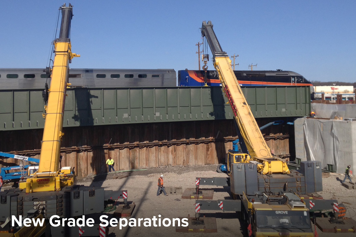 view of a Metra train passing over a newly built grade separation as construction continues on the roadway below