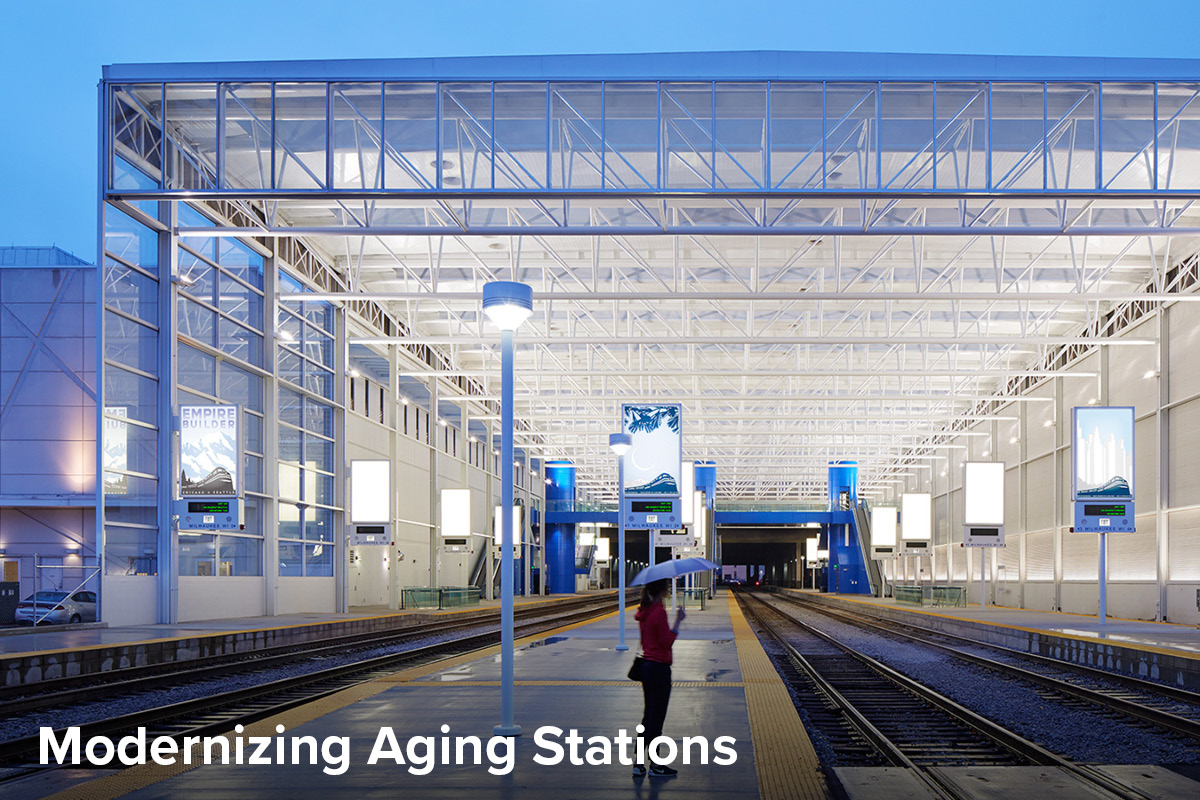 View of the new Milwaukee Train Shed at dusk, a woman with an umbrella stands on the fully-ADA-accessible platform waiting for a train