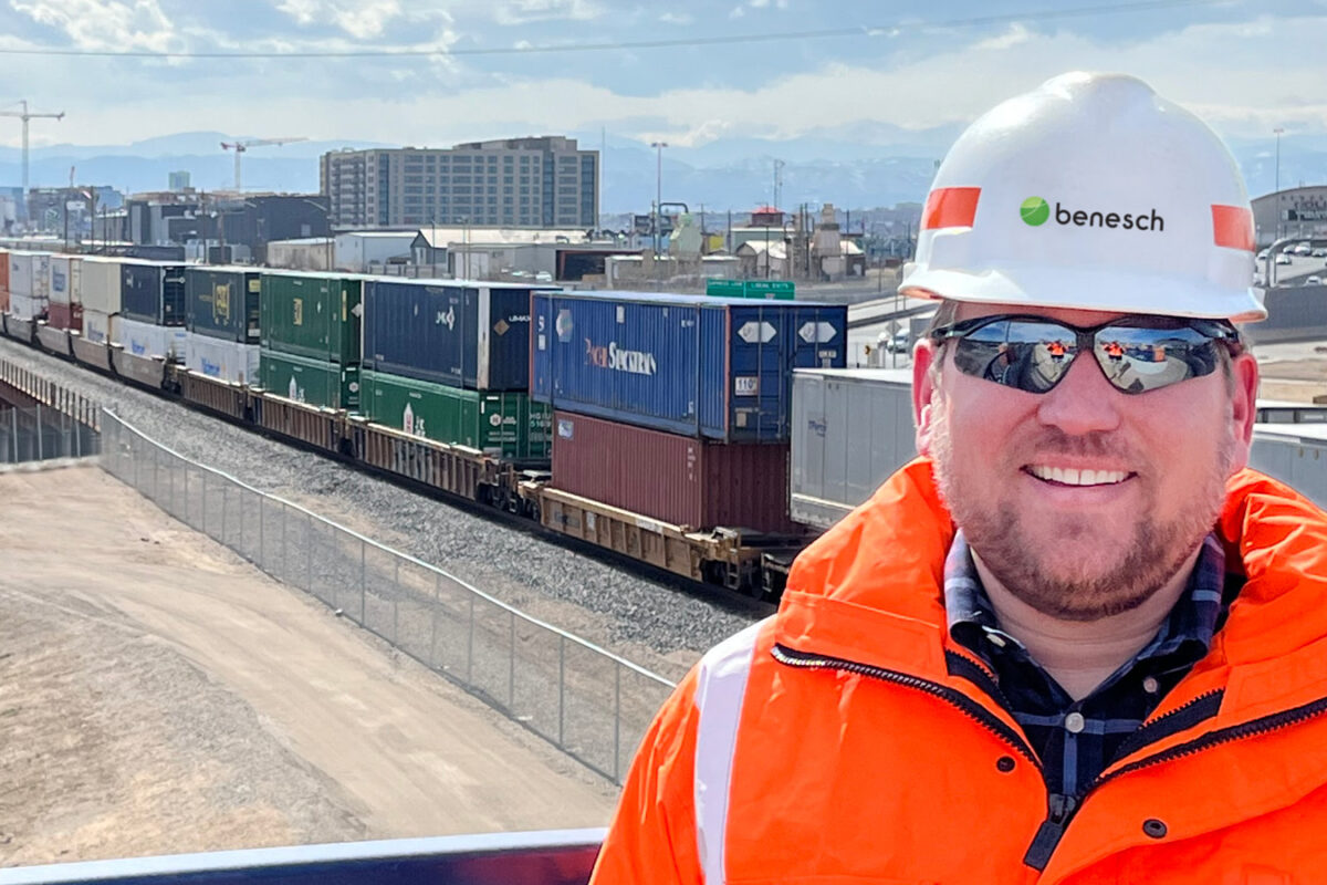 A photo of Jordan Card wearing a hard hat and orange jacket in the field