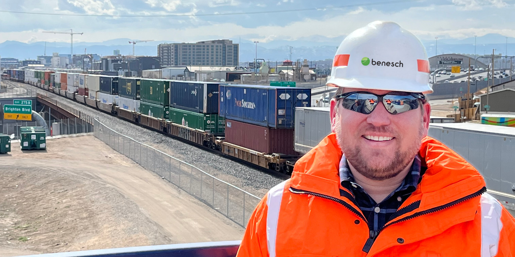 A photo of Jordan Card wearing a hard hat and orange jacket in the field