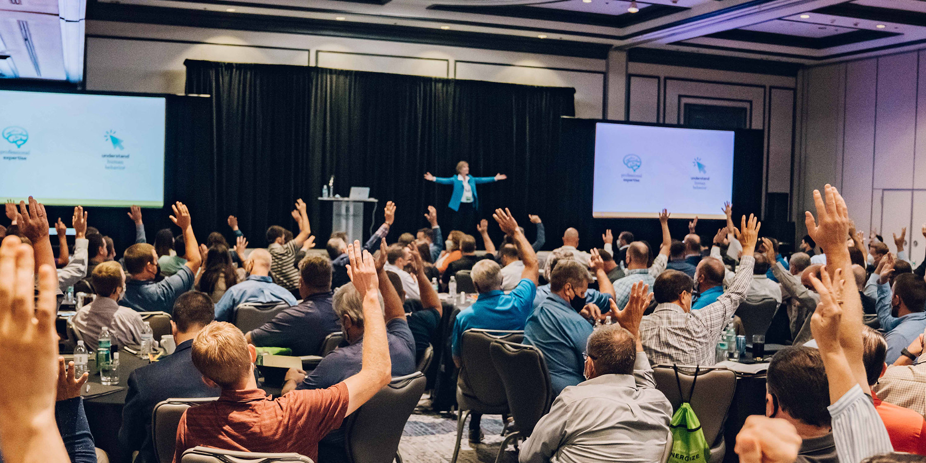 A photo of a managers training event hosted by Benesch - the presenter stands before a crowd of 200 employees with their hands raised