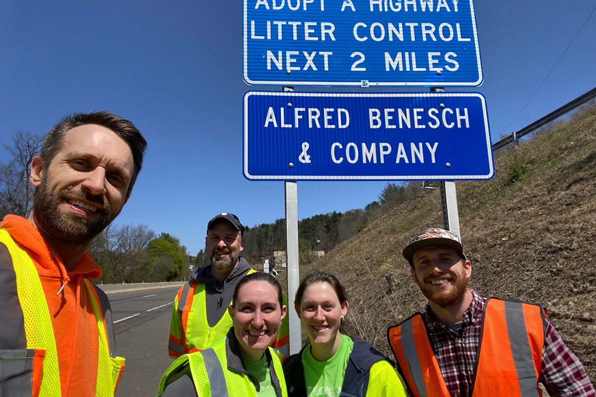 Benesch employees posing by an adopt-a-highway sign for the company after a day of trash pick-up