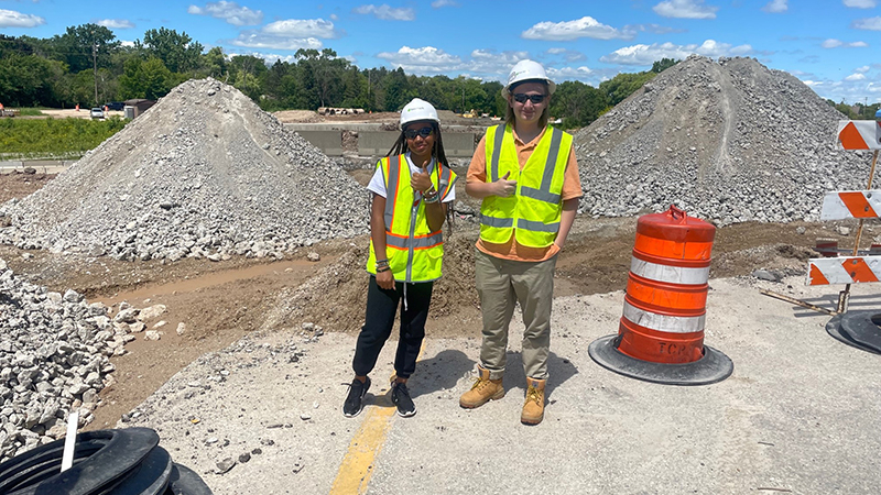 A photo of an engineer and an intern in front of piles of gravel smiling