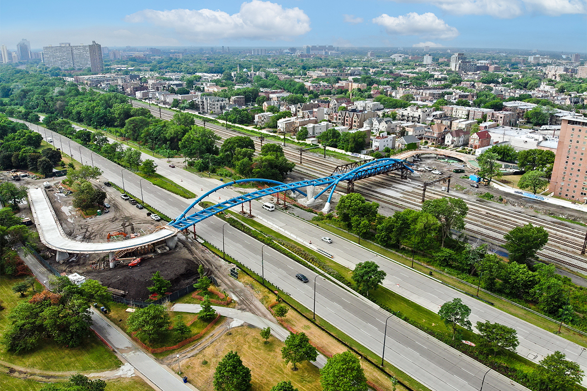 Aerial view of the new 43rd Street pedestrian bridge under construction, spanning Lakeshore drive and several railroad lines. The bridge is a blue asymmetrical arch bridge