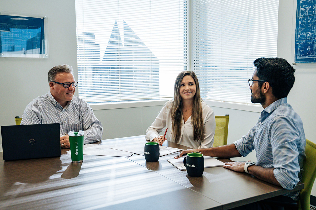 A photo of a manager and two employees talking and smiling in a conference room