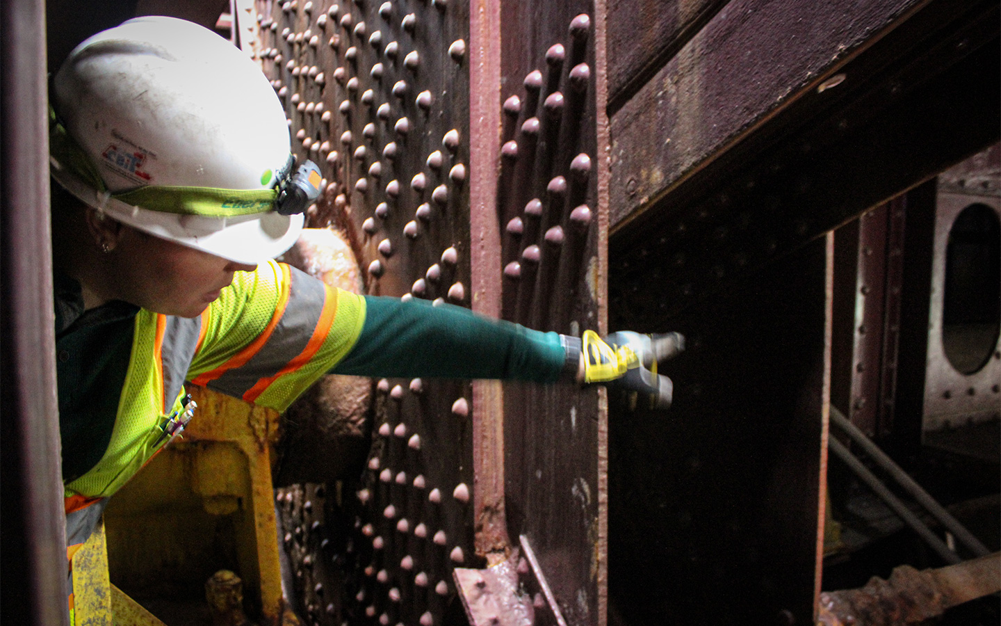 Photo of Benesch inspector squeezing in near the trunnion bearings to get a better view of the truss members and framing system spanning the counterweight pits.