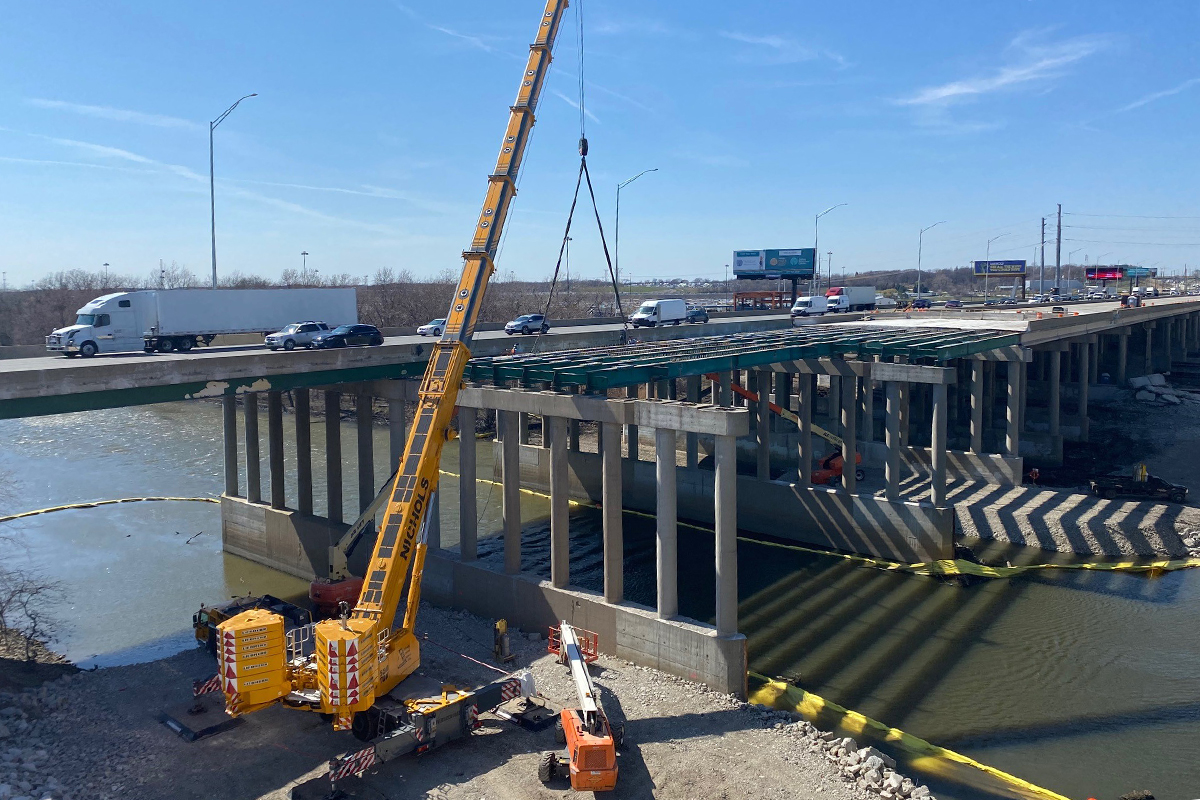 Construction view of the Mile Long Bridge spans being set over a waterway as traffic continues on the structure alongside it.