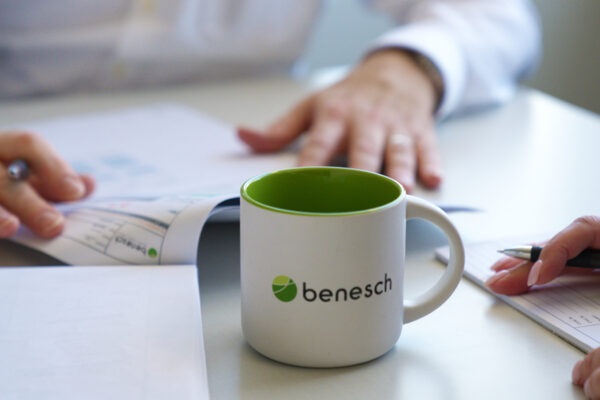 image of a set of plans on a table as two people look over them. A Benesch mug is in the foreground.