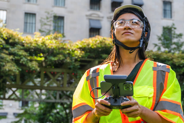 Woman in safety gear looking up while holding drone controller