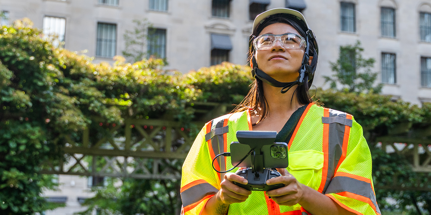 Woman in safety gear looking up while holding drone controller