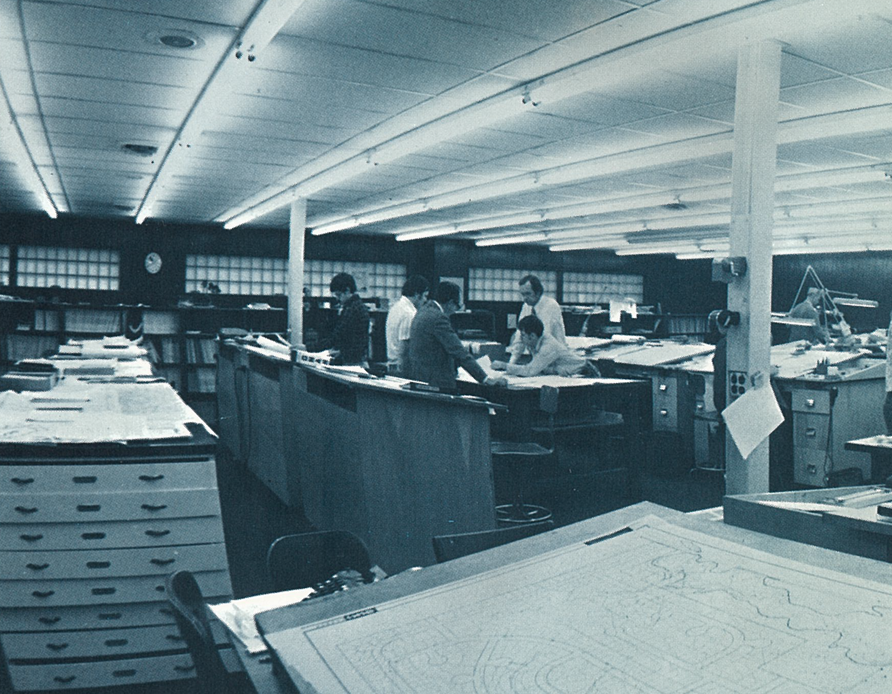 historic image of Benesch staff in an open office looking at plans