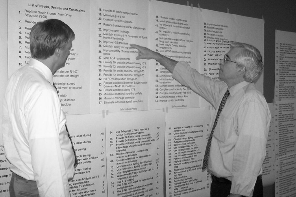 black and white photo of Benesch engineers reviewing Value Engineering study notes taped to a wall